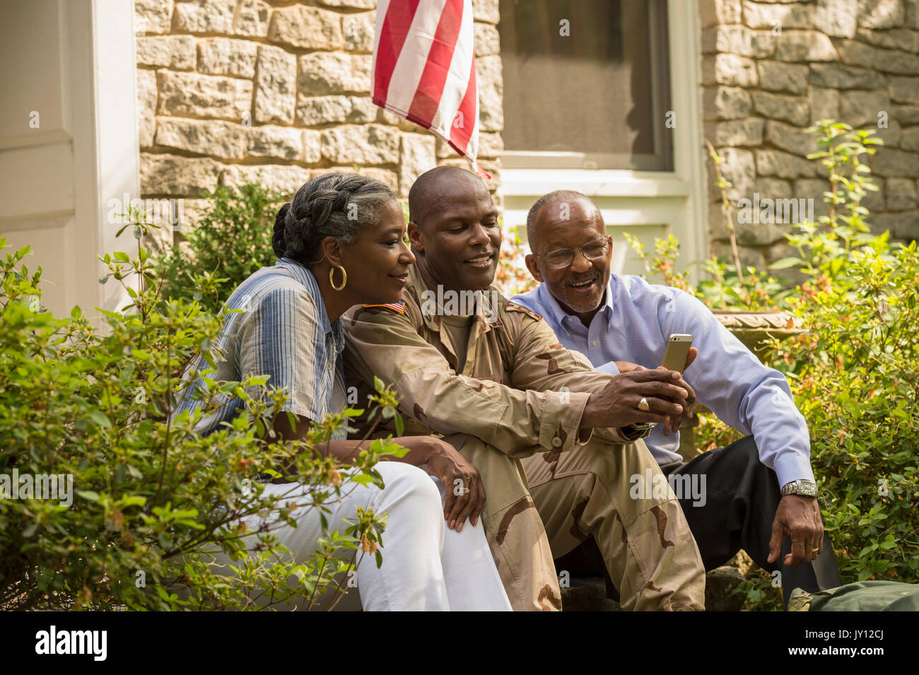 Soldat sitzt auf der vorderen Stoop mit Eltern und SMS auf Handy Stockfoto