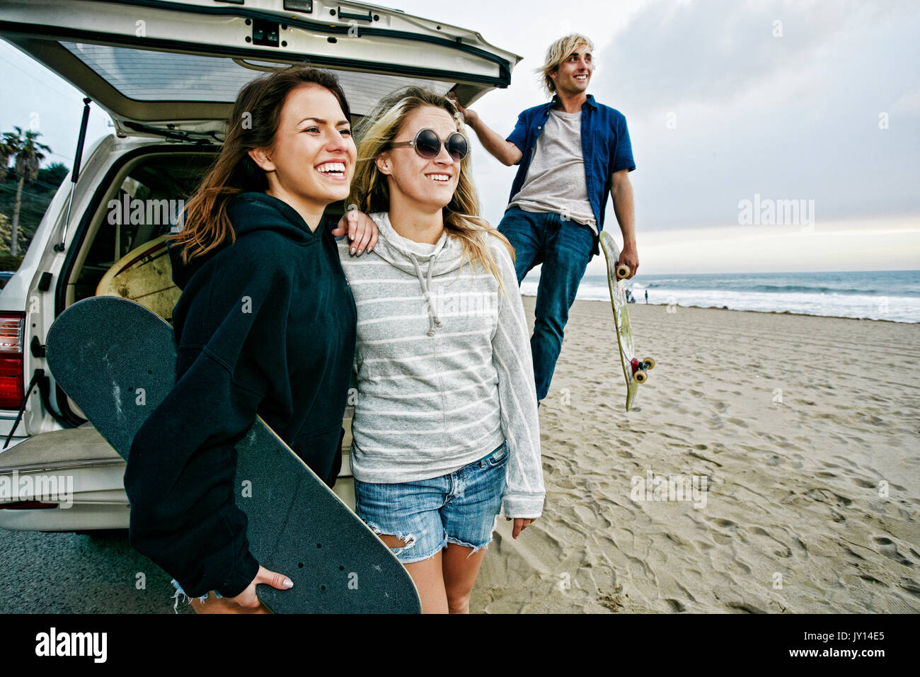 Kaukasische Freunden in der Nähe von Auto Limousine am Strand holding Skateboards Stockfoto