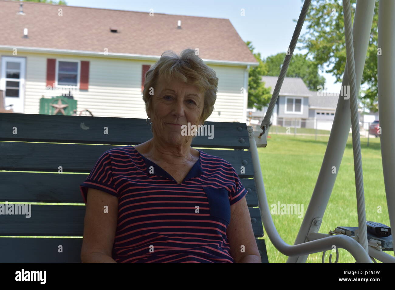 Ältere Frau auf einer Schaukel sitzend in ihrem Hinterhof Lächeln. Sie scheint nicht, eine Betreuung in der Welt an diesem schönen, sonnigen Tag zu haben! Stockfoto