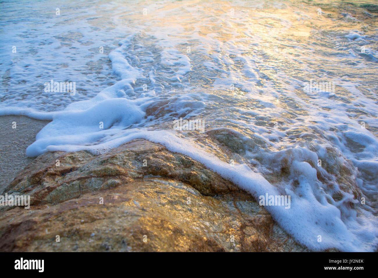 Weiche Wellen schlagen die Felsen mit Sonnenlicht Stockfoto