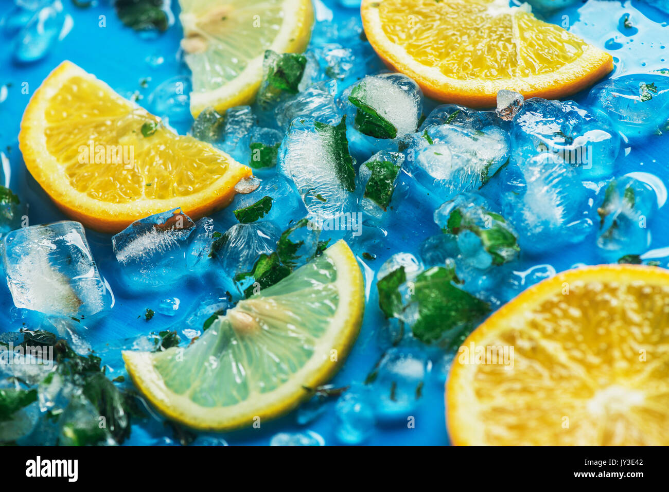 Close-up von geschnittenen Orangen und Zitronen auf blauem Hintergrund mit Eiswürfel Stockfoto