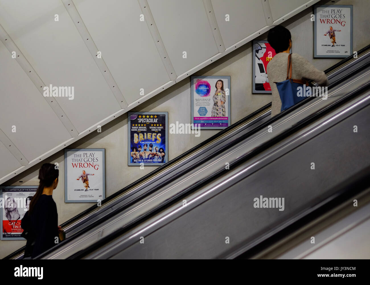 Passagiere lesen die Werbetafeln an der Wand der Rolltreppe an einer Londoner U-Bahn-Station Stockfoto
