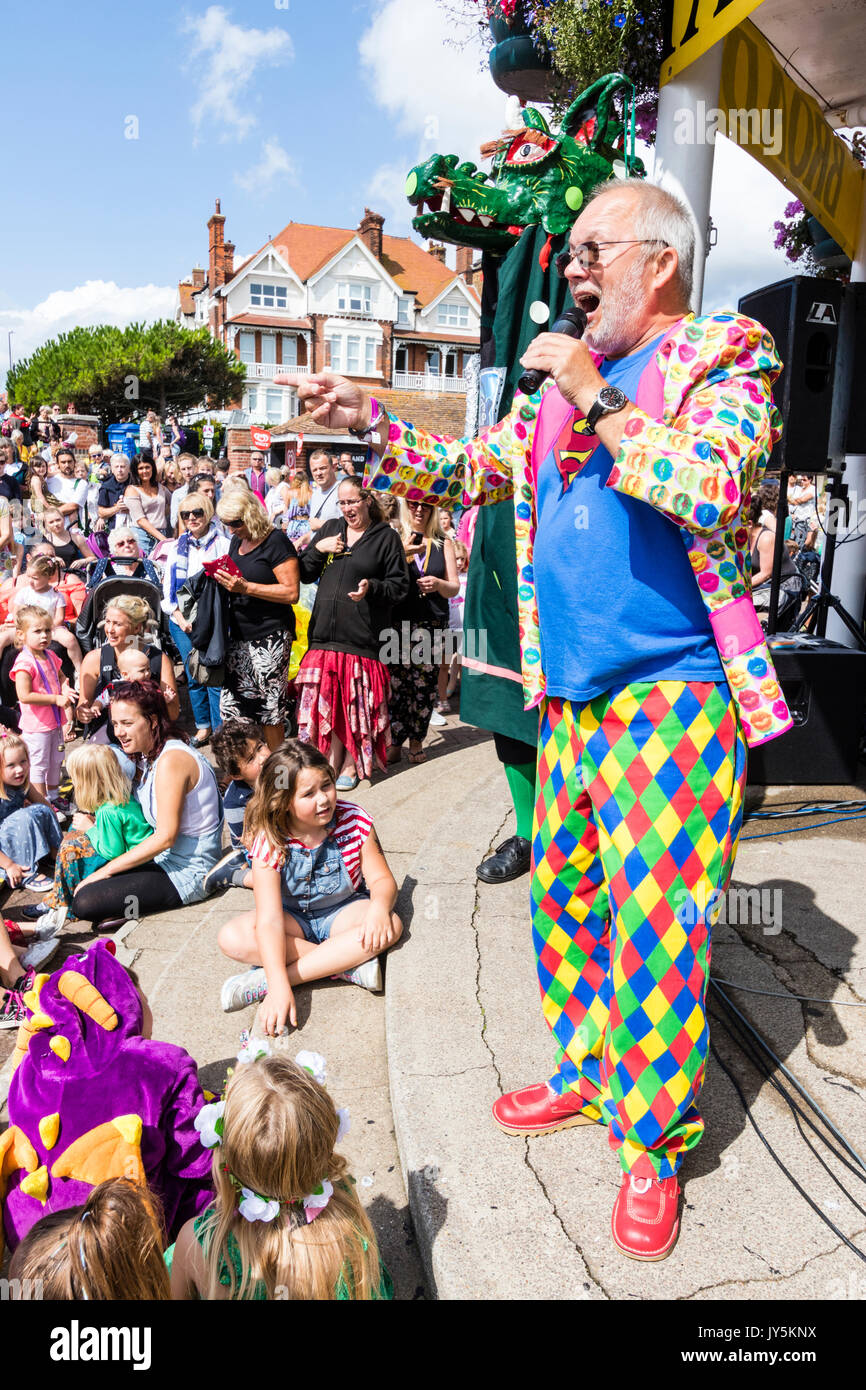 Moderator Mick Scott stehen auf musikpavillon vor der Masse von Eltern und Kindern während Broadstairs Folk Woche. Tragen bunte Jacke und Hose, hält ein Mikrofon sprechen. Stockfoto