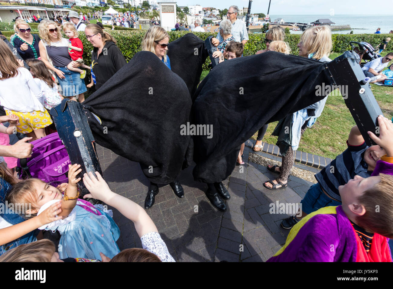 Hooded Pferde, Ossies, Symbol der Broadstairs folk Woche, umgeben von vielen kleinen Kindern, die bis zu berühren und Schlaganfall sind das schwarze Kostüm der mit Kapuze Pferde. Stockfoto