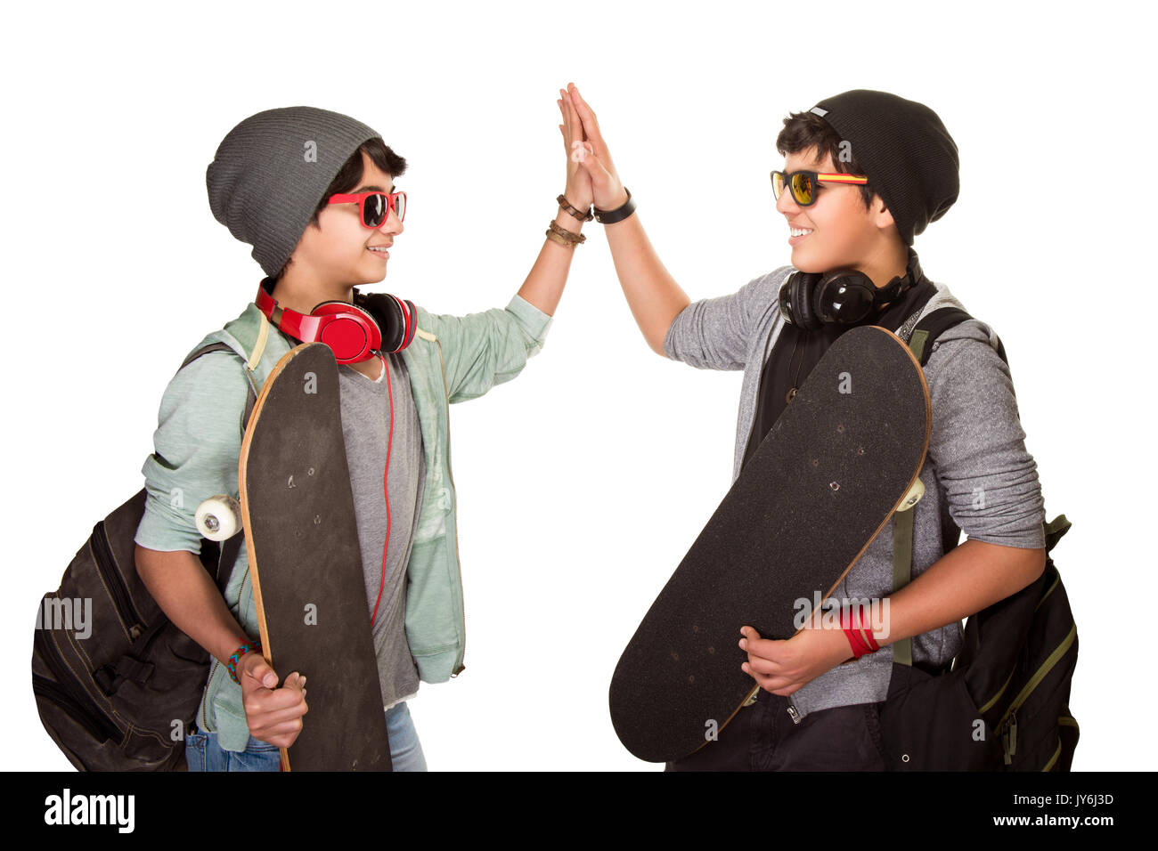 Zwei glückliche Skateboarder Technologiefeldes einander auf weißem Hintergrund, beste Freunde tragen elegante Hüte, Sonnenbrillen und hören Musik von Ohr Stockfoto