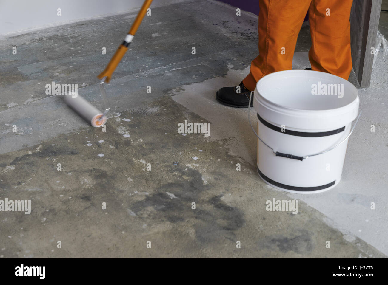 Haus im Bau. Arbeitnehmer setzt Grundierung mit Walze auf Betonboden Stockfoto