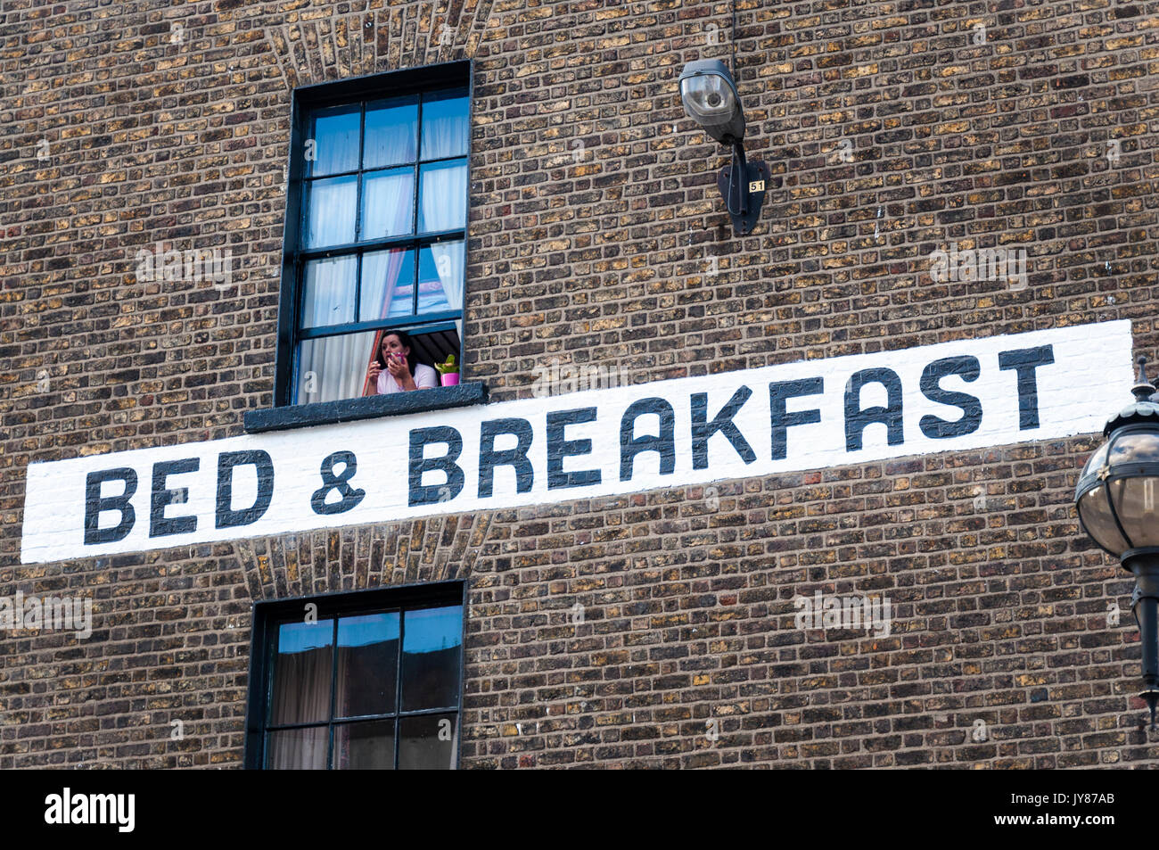 Eine Frau rauchen Mit smart phone sieht aus dem Bett und Frühstück Fenster auf Talbot Street in Dublin, Irland Stockfoto