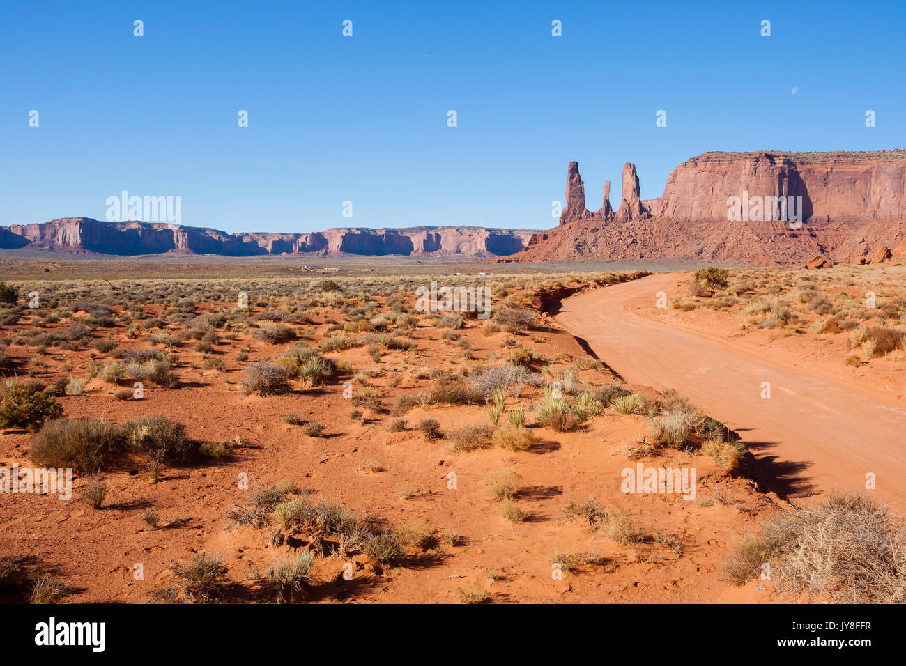 Monument Valley, Utah, USA. Schmutz Straße, die zu den Drei Schwestern Rock gegen den blauen Himmel. Stockfoto