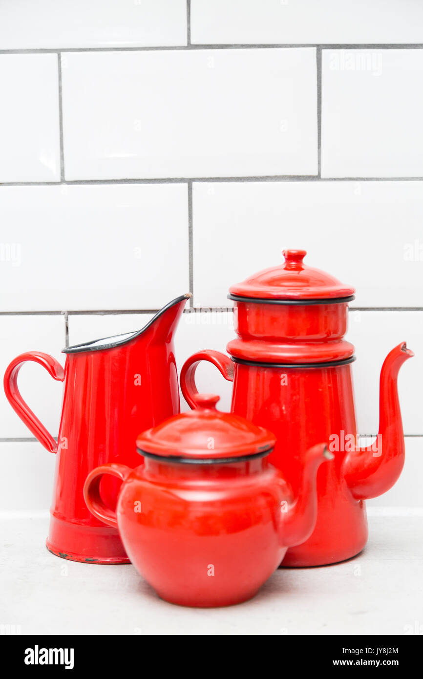 London, Großbritannien. Rot-weißes Email Wasserkrug, Teekanne und Kaffeekanne gegen weiße Fliesen Hintergrund. Stockfoto
