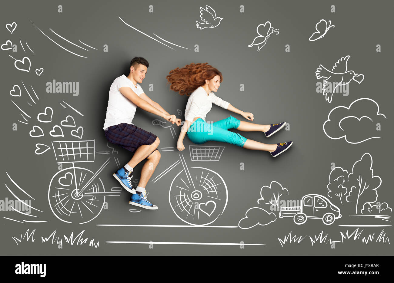 Happy Valentines Love Story Konzept für ein romantisches Paar, das Fahrrad gegen Kreidezeichnungen Hintergrund. Stockfoto