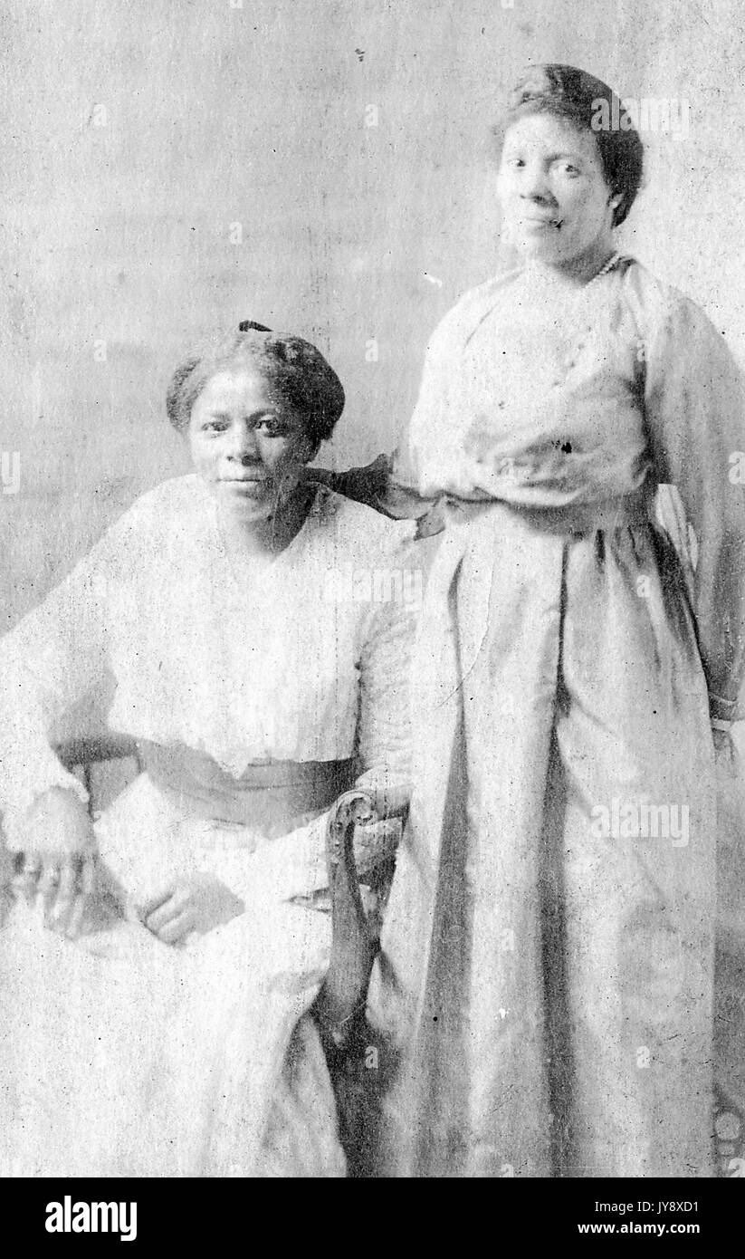 Ganzkörperportrait von zwei reifen afroamerikanischen Frauen, eine Frau sitzend, eine Frau stehend, beide in leichten Kleidern, neutraler Ausdruck, 1915. Stockfoto