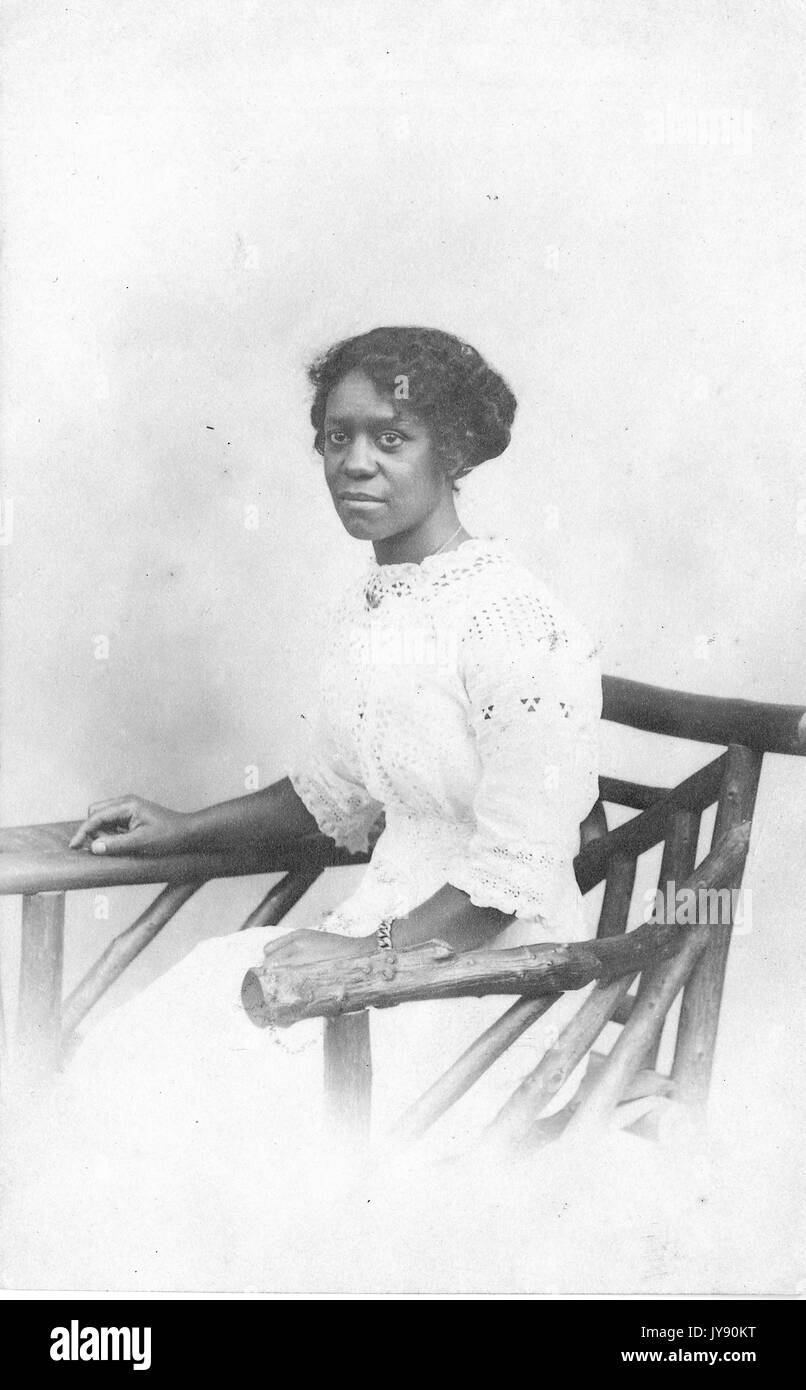 Portrait einer afrikanischen amerikanischen Frau sitzt in einer Hand - geschnitzte hölzerne Stuhl, trug ein weißes Kleid, Willow Grove Park, Pennsylvania, 1915. Stockfoto