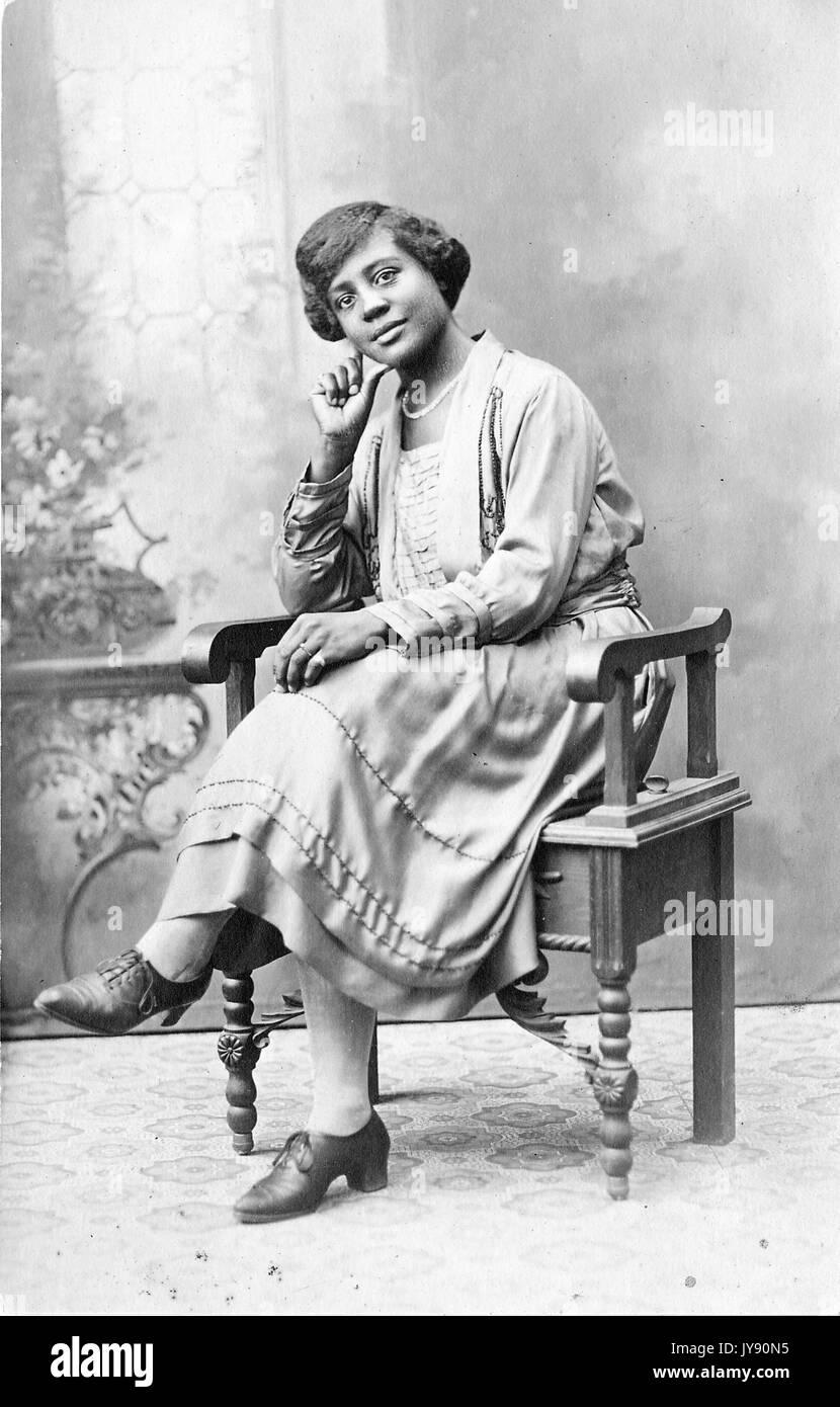 Portrait einer afrikanischen amerikanischen Frau in einem holzstuhl saß, trug ein Kleid, 1915. Stockfoto