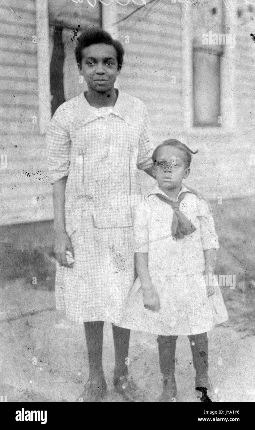 Porträt von zwei afrikanischen amerikanischen Geschwister, beide junge Mädchen tragen hellen Outfits, das ältere Mädchen ihre Hand auf die Schulter des jüngeren Mädchen, 1920. Stockfoto