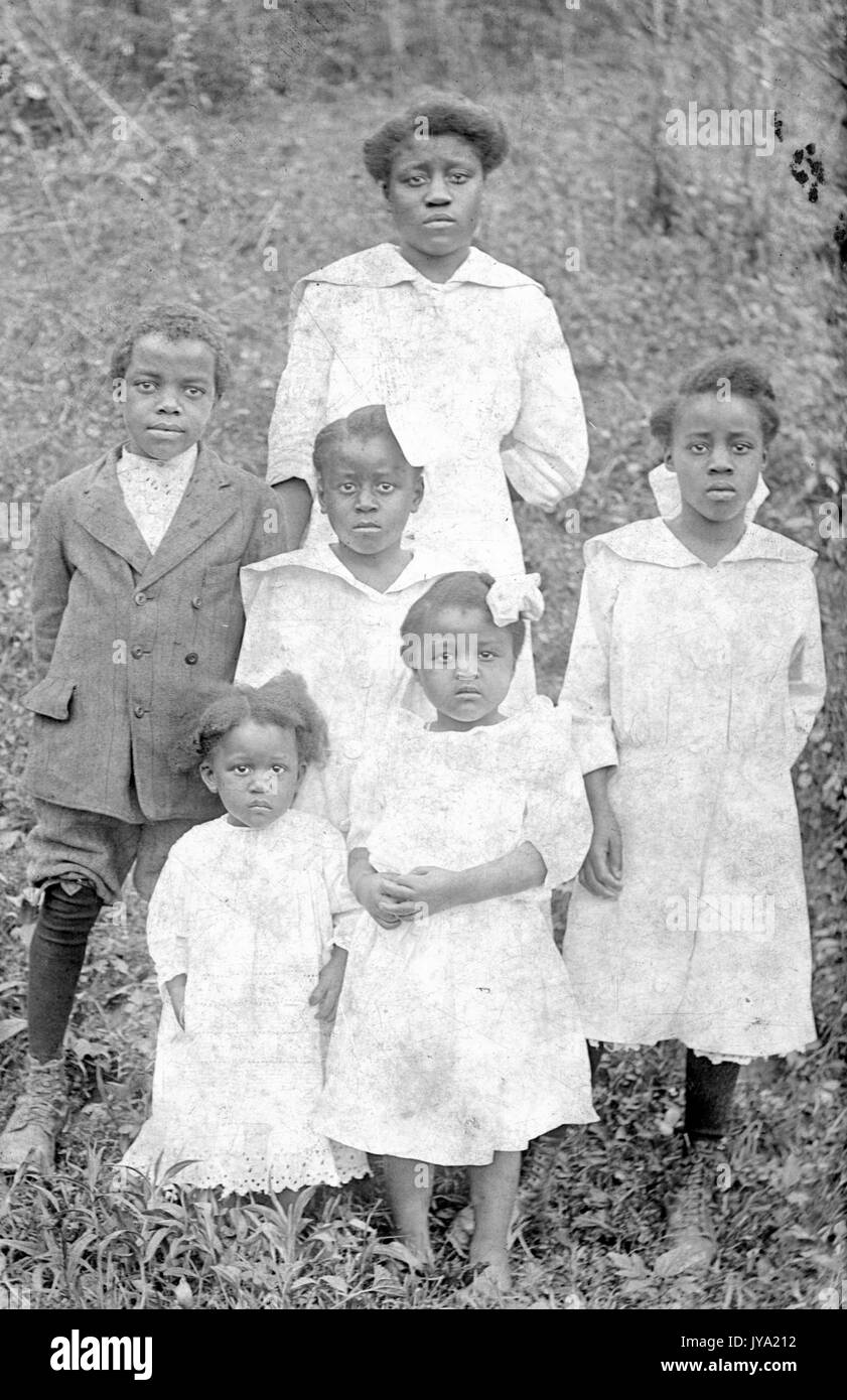 Portrait einer afrikanischen amerikanischen Mutter und ihre fünf Kinder stehen auf einem grasbewachsenen Hügel, alle Mädchen sind in hellen Kleidern und der Junge in einen dunklen Anzug, 1920. Stockfoto