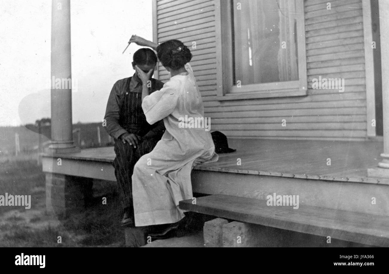 Afrikanische amerikanische Mutter mit ihrem Kind sitzen auf der Veranda einer Plantage Stil zu Hause, mit einem Rasiermesser die childs Haare schneiden zu lassen, halten Sie die childs Kopf in ihre Hand und strich mit dem Rasiermesser, 1932. Stockfoto