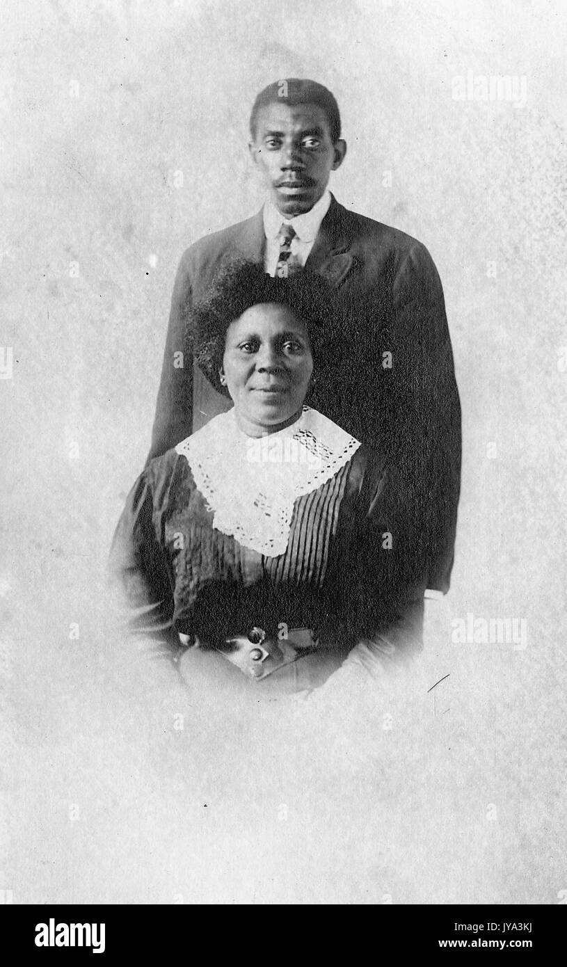 Reifen Afrikanische amerikanische Paar, ein Mann und eine Frau, die Frau vor dem Mann mit dem Kleid sitzt, der Mann stehen und in Anzug, im ursprünglichen Foto, 1932 abgeschnitten. Stockfoto