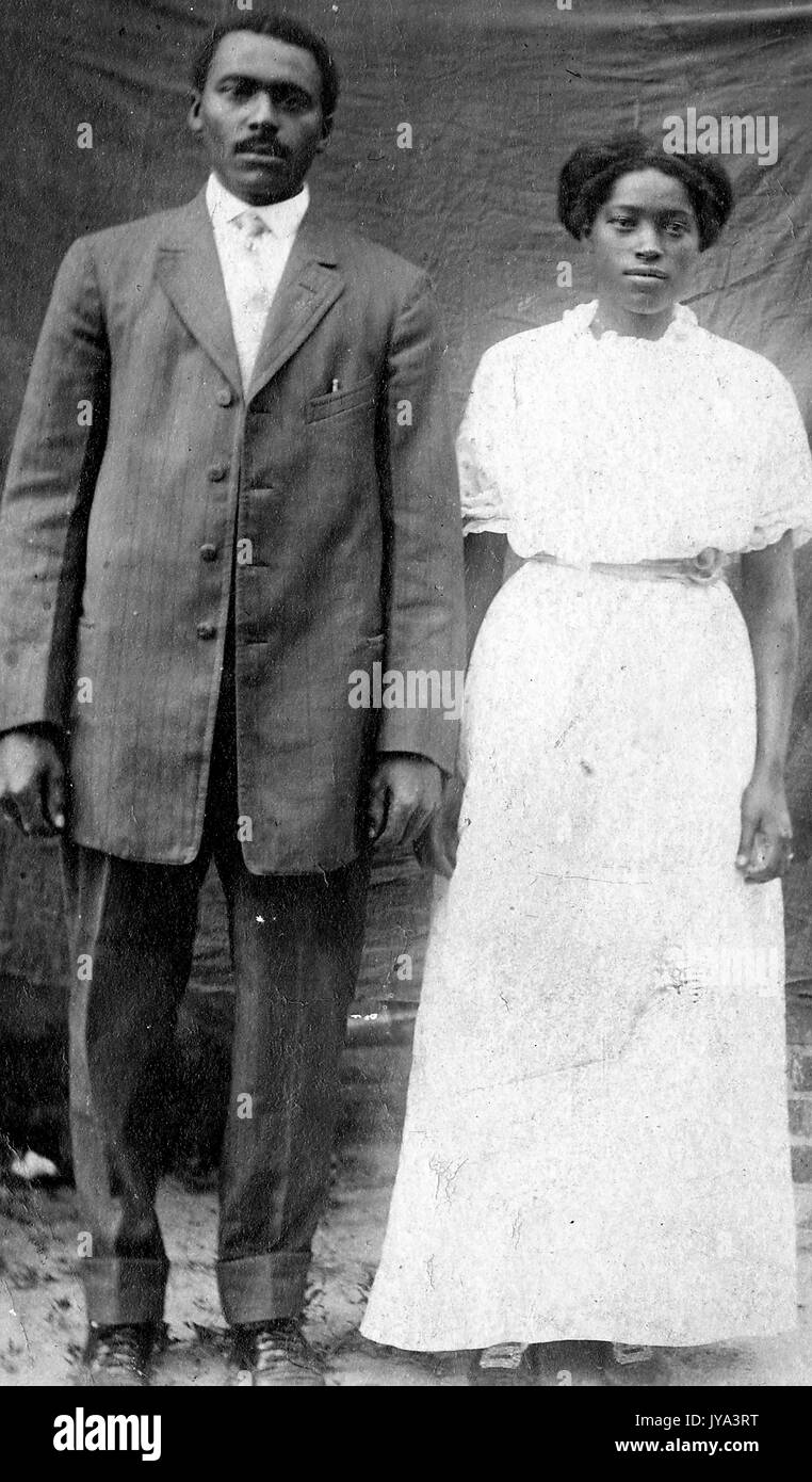 Afrikanische amerikanische Paar für Fotografien vor ein hängendes Blatt posieren, die Frau trägt ein weißes Kleid, Mann in Anzug und Krawatte, 1915. Stockfoto