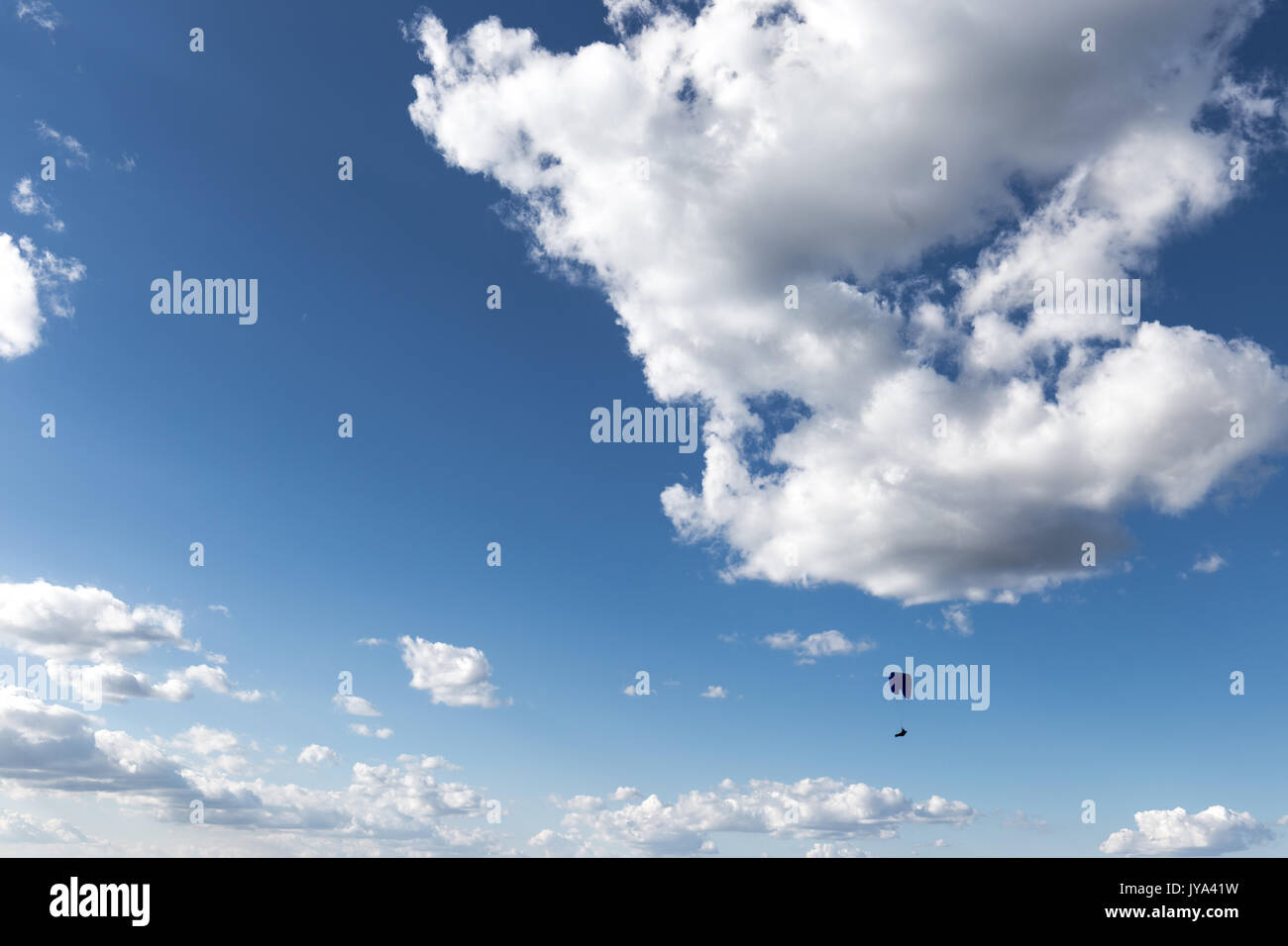 Ein Gleitschirm gegen einen tiefen, blauen Himmel fliegen, mit großen weißen Wolken Stockfoto