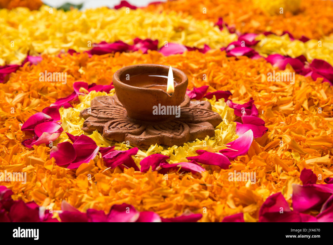 Blume rangoli für Diwali oder pongal mit Ringelblume oder zendu Blumen und roten Rosenblättern über weißen Hintergrund mit diwali Diya in der Mitte, Sel Stockfoto