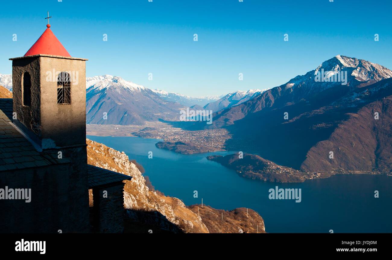 Die Kirche von Saint Bernard und ihrem Glockenturm in Musso, entlang der Monti Lariani weg. Im Hintergrund, den Comer See und Bassa Valtellina mit Berg L Stockfoto