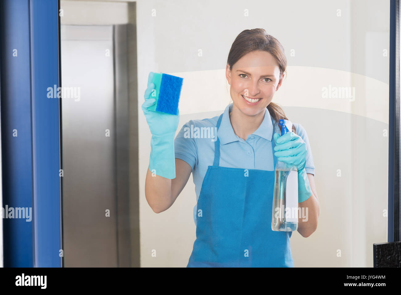 Junge Glücklich weiblichen Hausmeister Reinigung von Glas mit Waschmittel Sprühflasche und Schwamm Stockfoto