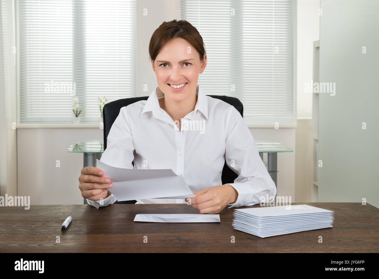 Junge glücklich Geschäftsfrau Holding Dokument mit Stapel Briefumschläge am Schreibtisch im Büro Stockfoto