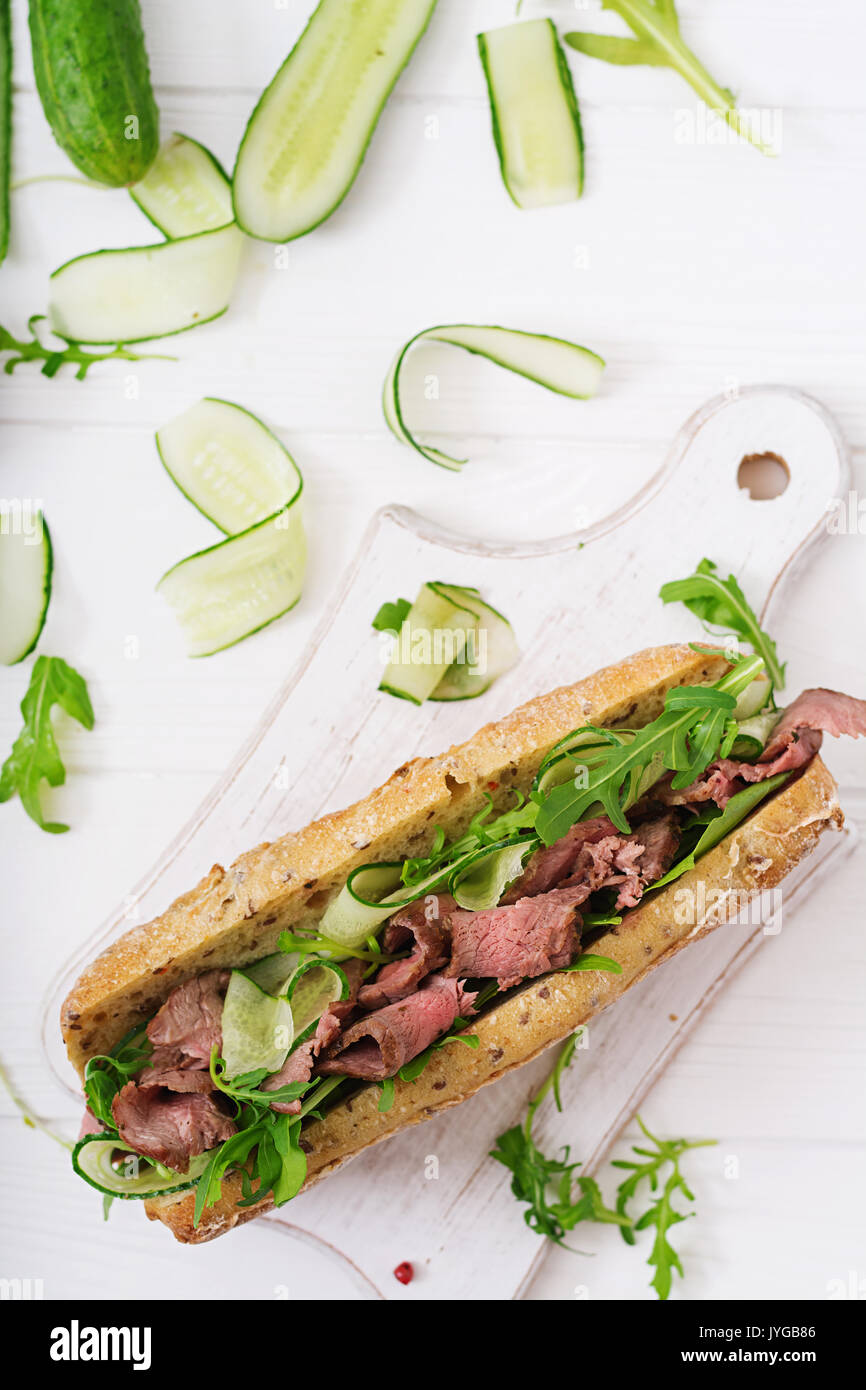 Sandwich von Vollkornbrot mit Roastbeef, Gurke und Rucola. Ansicht von oben. Flach Stockfoto