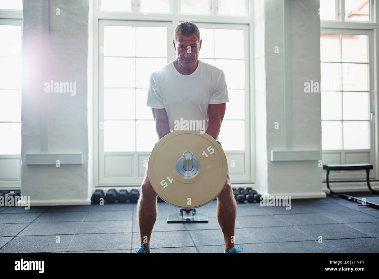 Porträt eines reifen Mannes in Sportkleidung alleine stehen in einer Turnhalle auf Gewichte während eines Trainings konzentriert Stockfoto