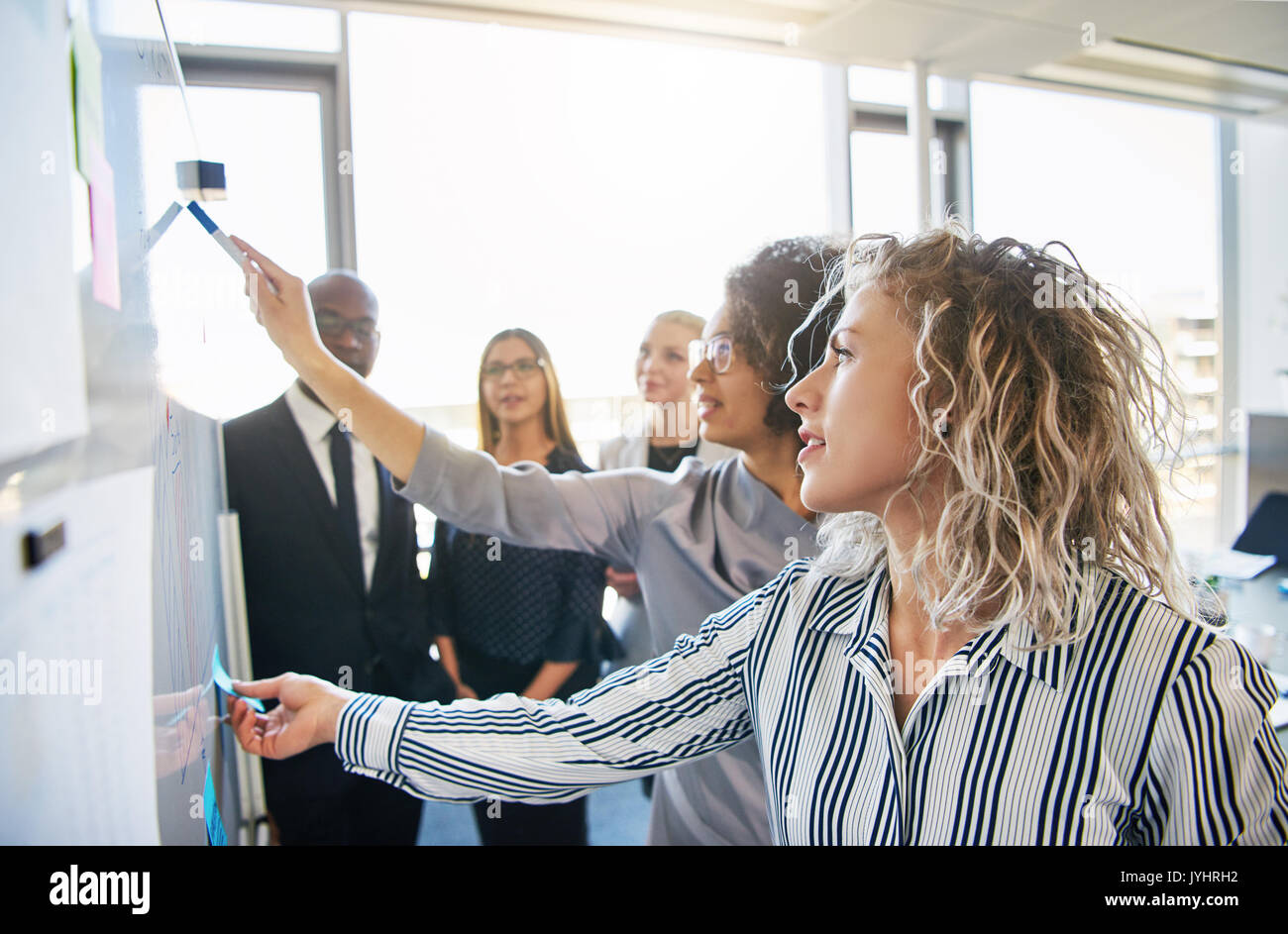 Gruppe der fokussierten Kollegen gemeinsam Brainstorming auf einem Whiteboard während einer Strategie Sitzung in einem hellen, modernen Büro Stockfoto