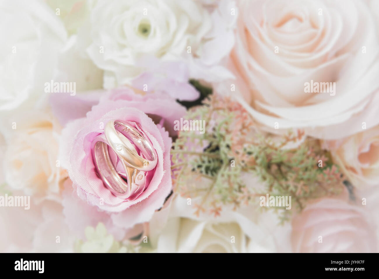 Zwei Trauringe mit Diamant auf Blumenstrauß Hintergrund Stockfoto