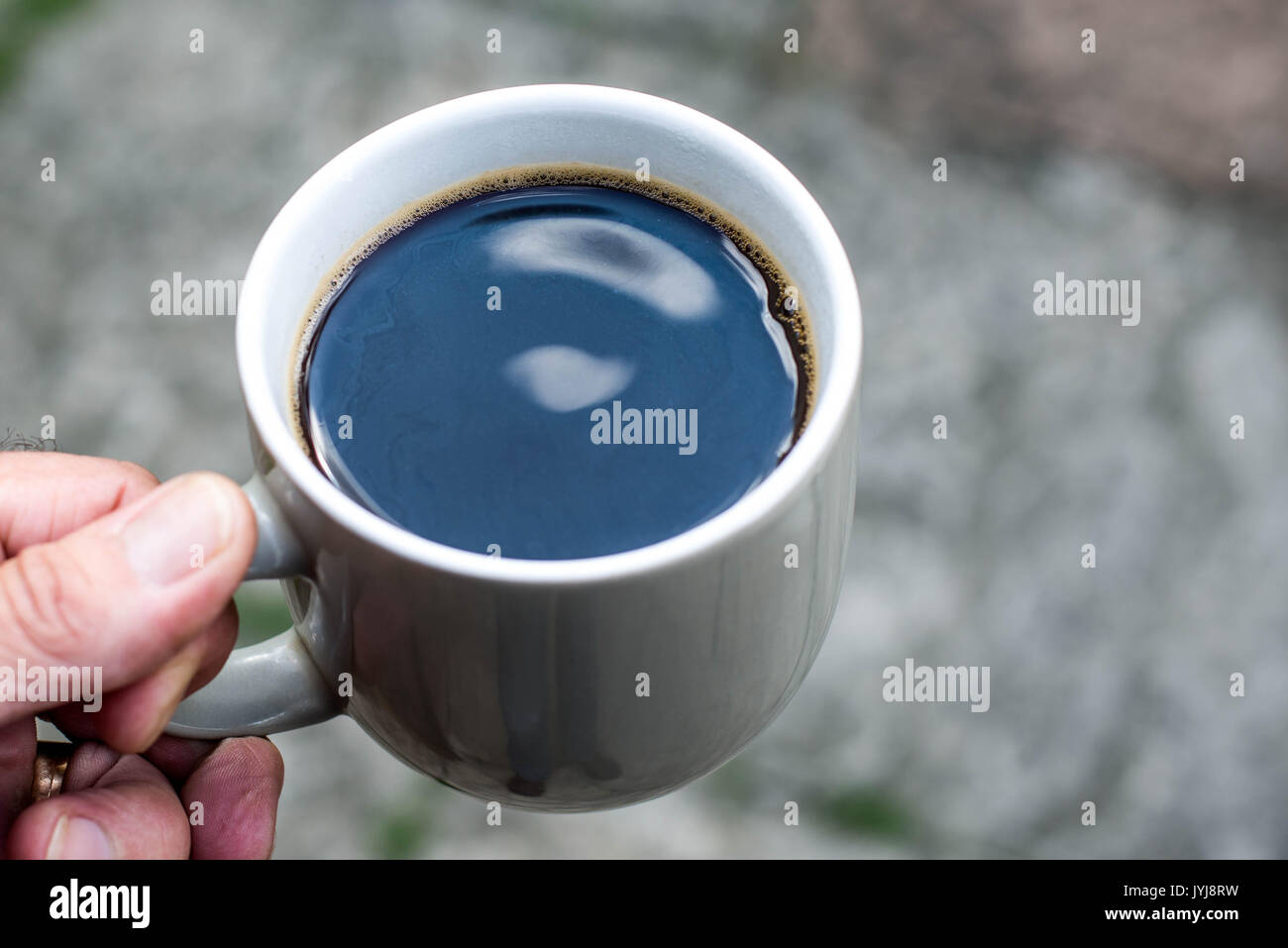 Mann hält eine Tasse schwarzen Kaffee vor einem dunklen Hintergrund Stockfoto