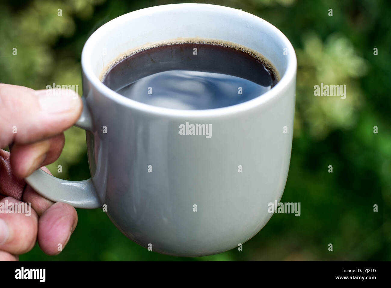 Mann hält eine Tasse schwarzen Kaffee vor einem grünen Hintergrund Stockfoto