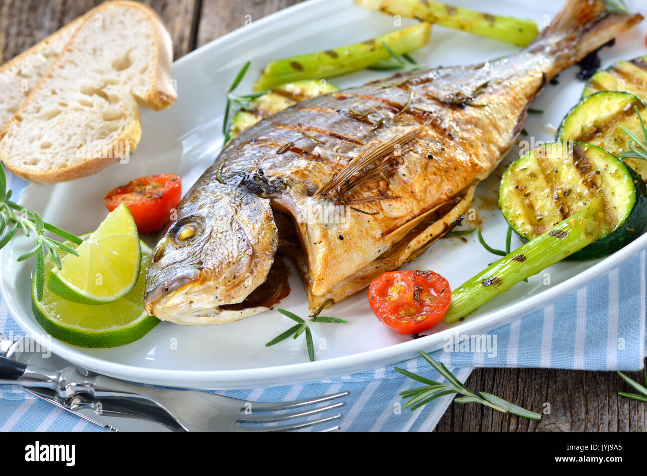 Gegrillte Goldbrasse mit gemischten Rosmarin Gemüse auf einer ovalen weißen Fischplatte serviert. Stockfoto