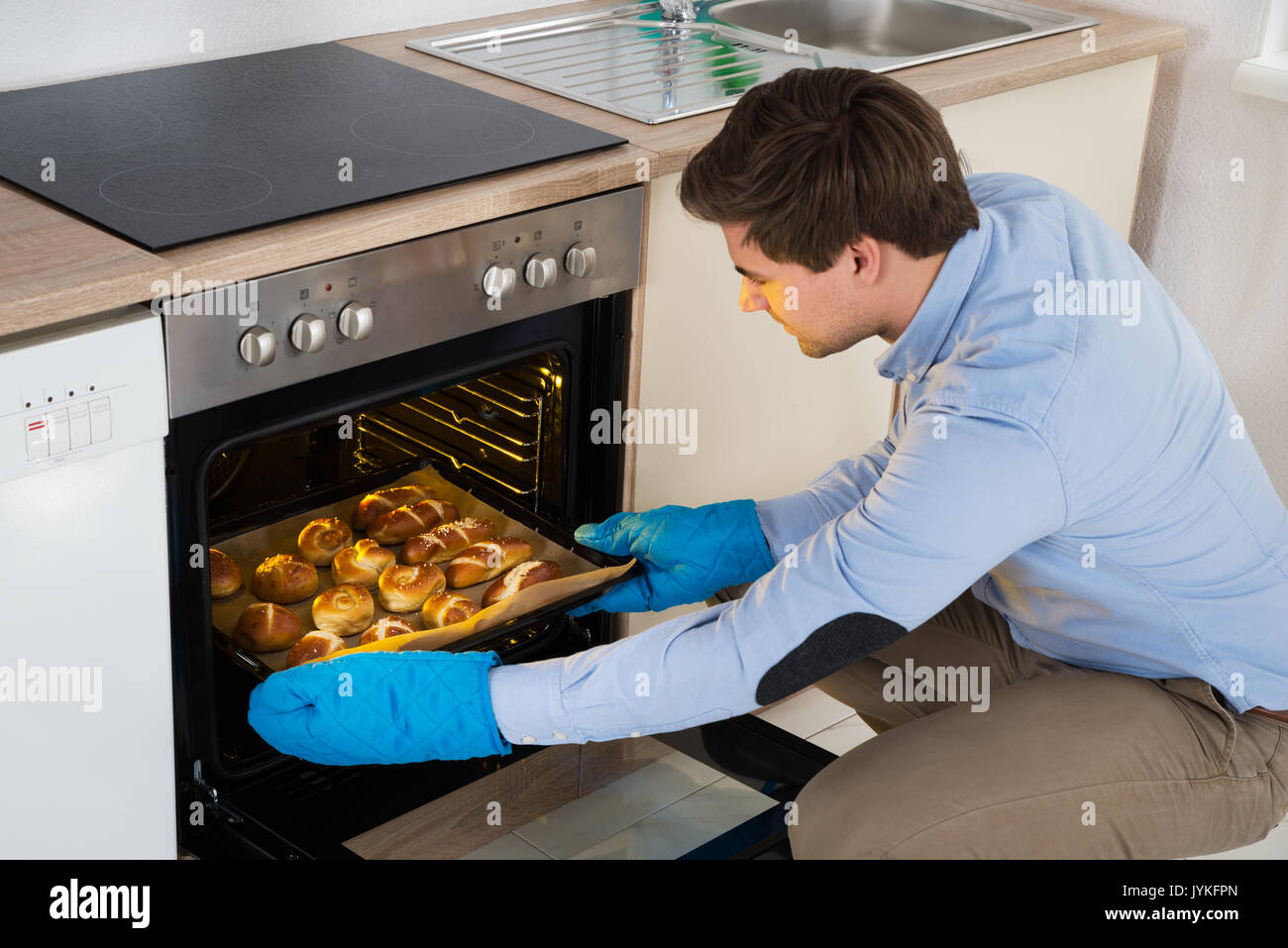 Junger Mann, Backblech, mit gebackenem Brot aus dem Ofen in der Küche Stockfoto