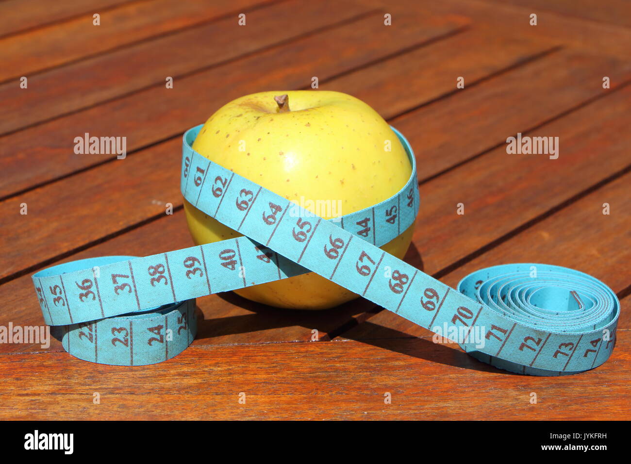 Maßband um einen goldenen Apfel auf einem Holztisch Stockfoto