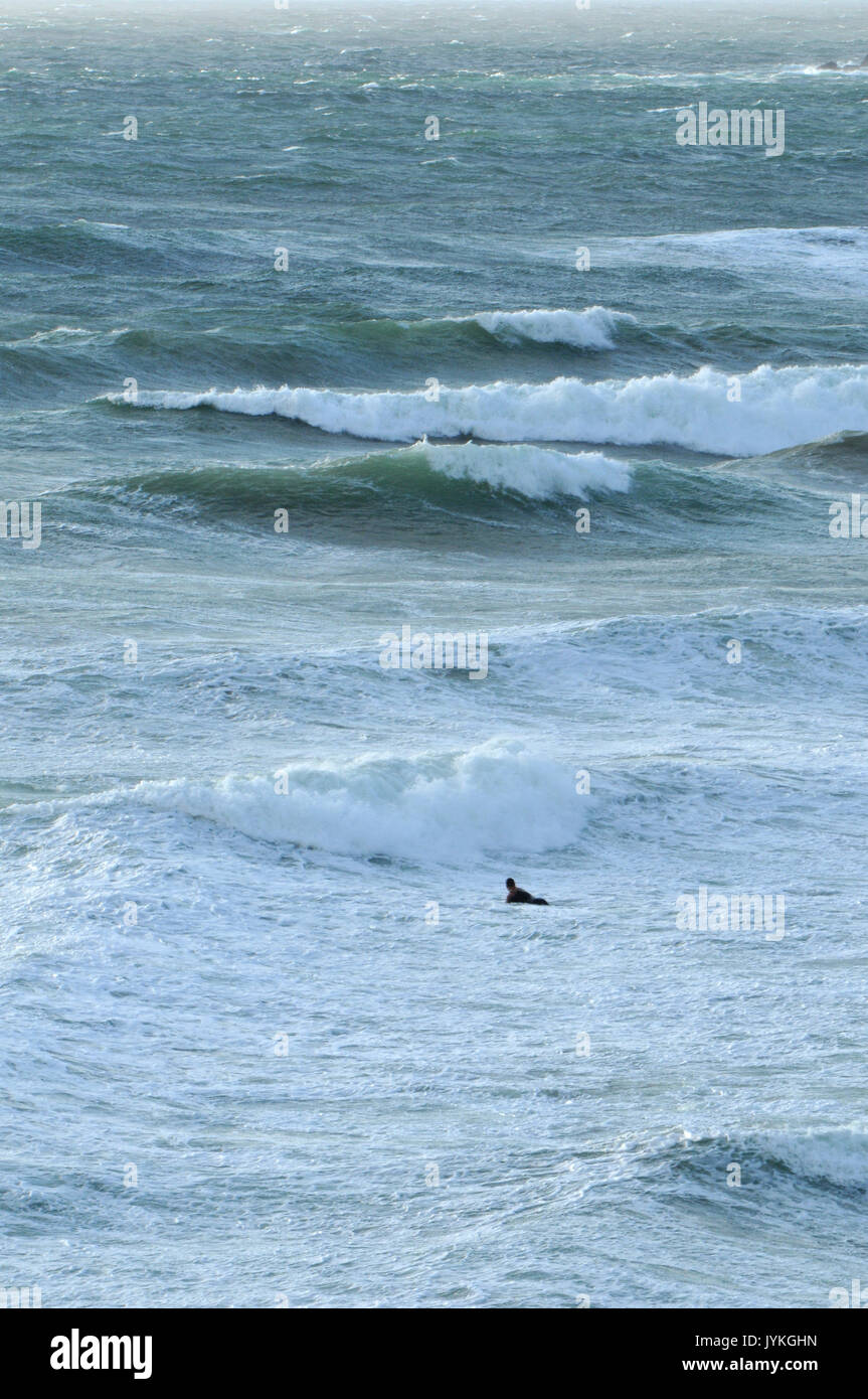 Ein einsamer Surfer trotzen die Wellen und die Brandung Brandung am Polzeath an der Küste von North Cornwall nur Surfer im Meer das Tragen von Neoprenanzug rauhes Wetter Stockfoto