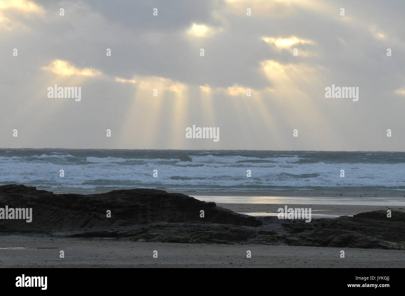 Ein Wolkenbruch Sonnenuntergang über polzeath Strand in North Cornwall in der Nähe des Camel Mündung Lichtstrahlen, die von den Wolken über dem Meer und Surfer Stockfoto