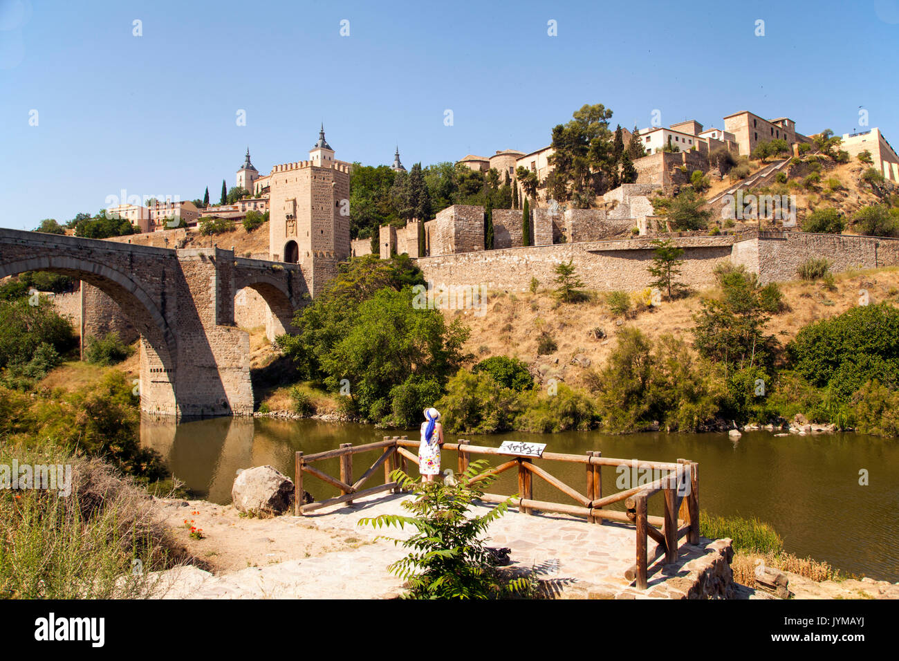 Frau mit Blick auf die Stadtmauern von Toledo Spanien über den Fluss Tejo mit Alcantara Bridge und dem Alcazar im Hintergrund Stockfoto