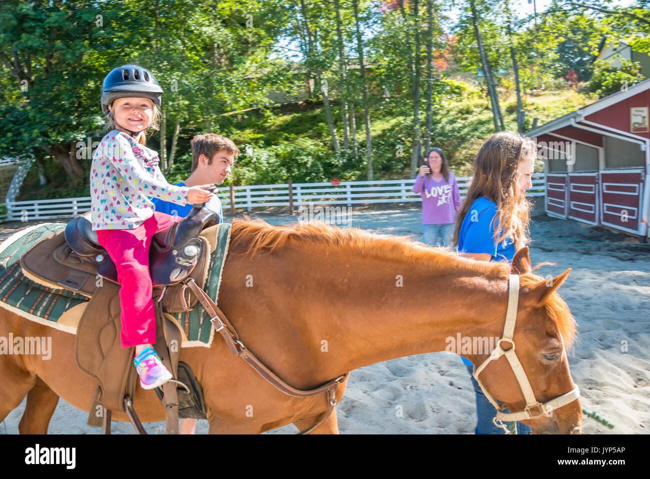 Kleines Mädchen, ein Pony reiten mit Großmutter unter Foto mit Smartphone gegeben Stockfoto