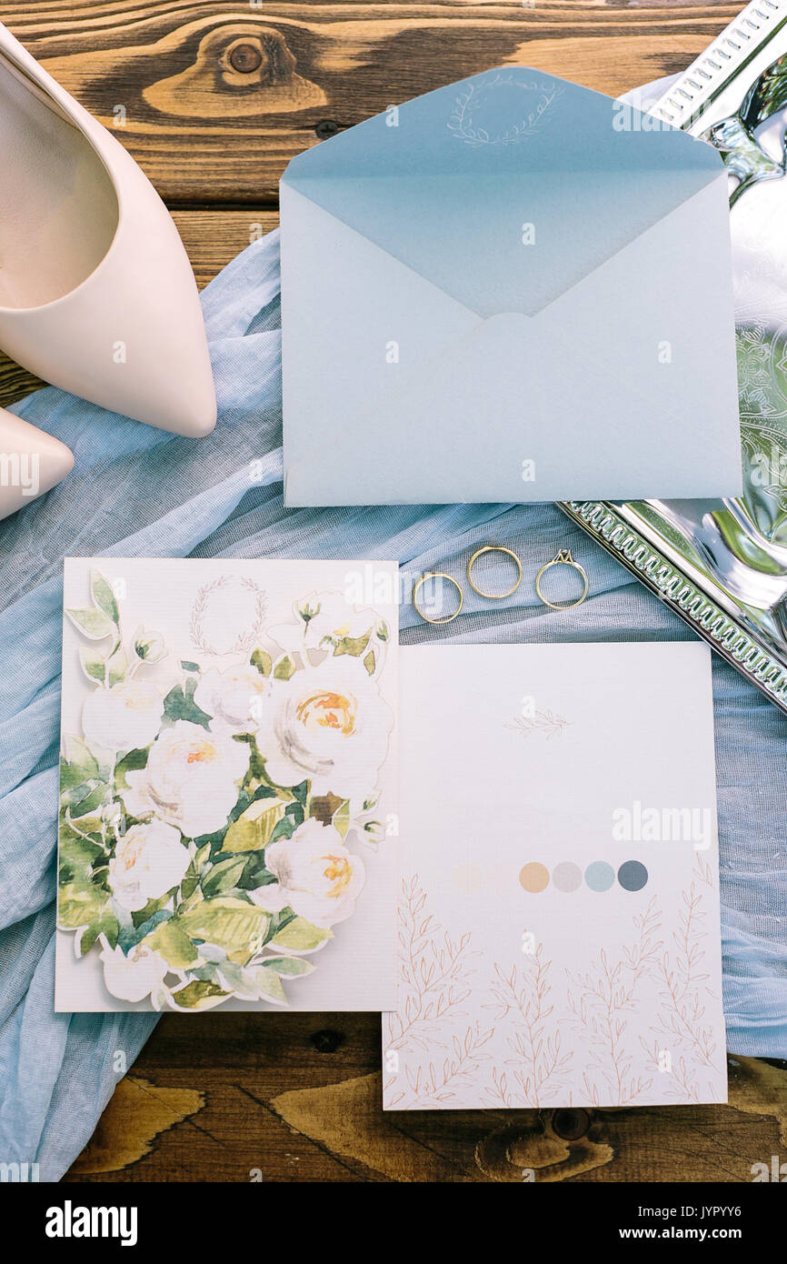 Zubehör, Ehevertrag, Zärtlichkeit Konzept. Herrliche flatlay von Pastelltönen. Es ist hellblau Kuvert Brief, zwei Postkarten mit floralem Design. Drei goldene Ringe und rosa Schuhe der Braut. Stockfoto