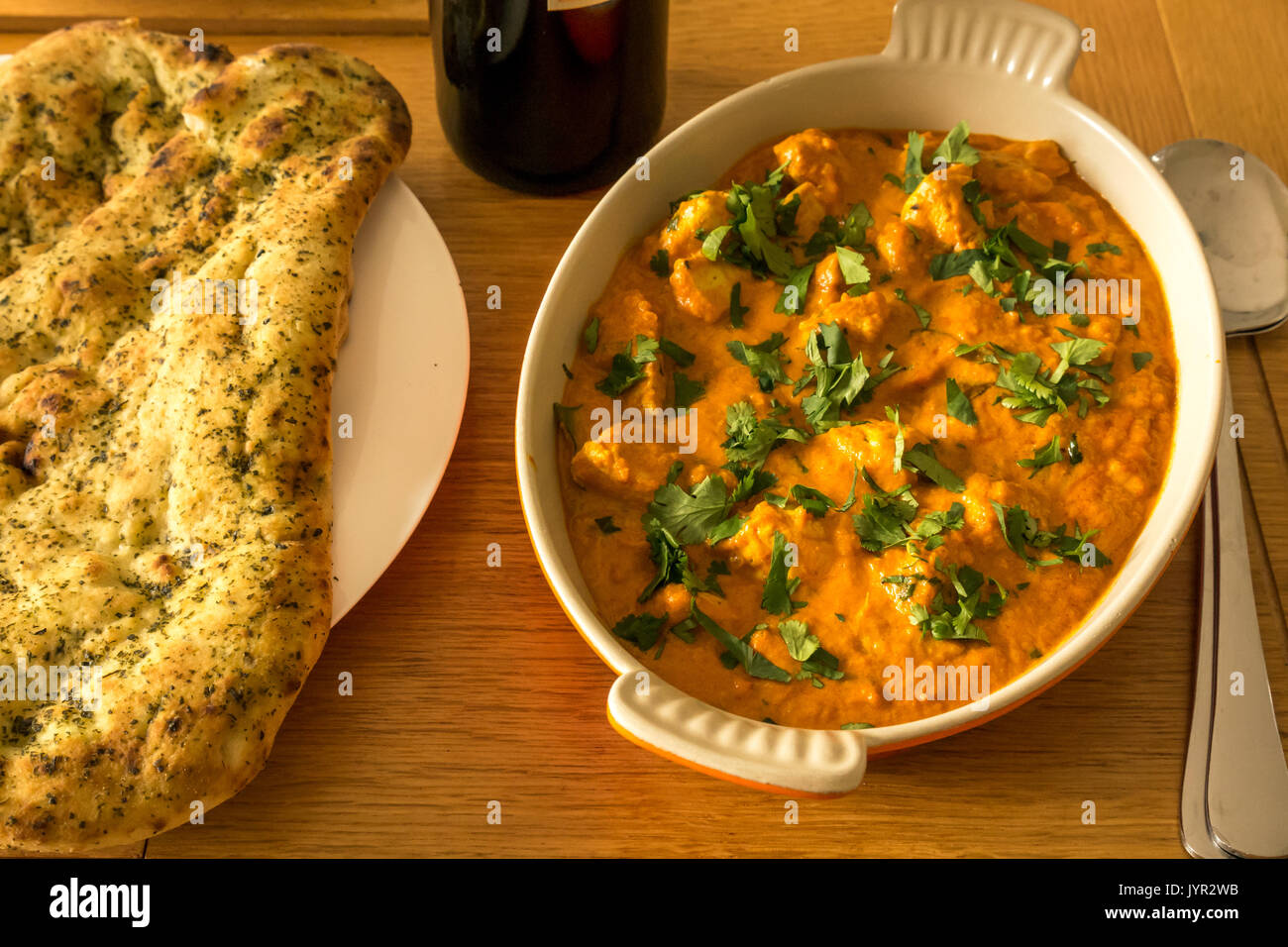 In der Nähe der Schüssel vom Huhn mit Naan Brot und eine Flasche Rotwein auf Eiche Tisch curry Stockfoto