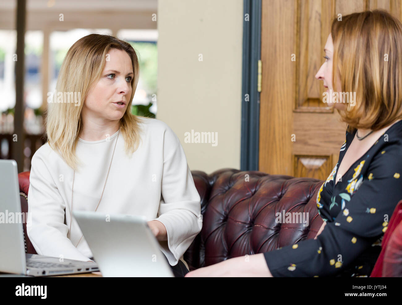 Zwei junge Unternehmerinnen sitzen auf einem Ledersofa in informelles Geschäftstreffen. Low Angle Perspektive mit selektiven Fokus auf explizite Gesicht. Horizont Stockfoto