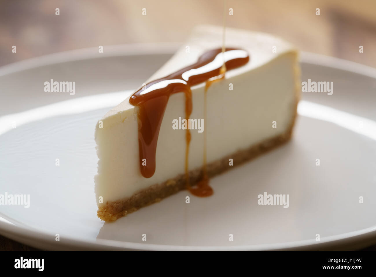 Karamellsauce auf Scheibe des traditionellen New York Cheesecake auf weiße Platte auf Holz Tabelle gegossen Stockfoto