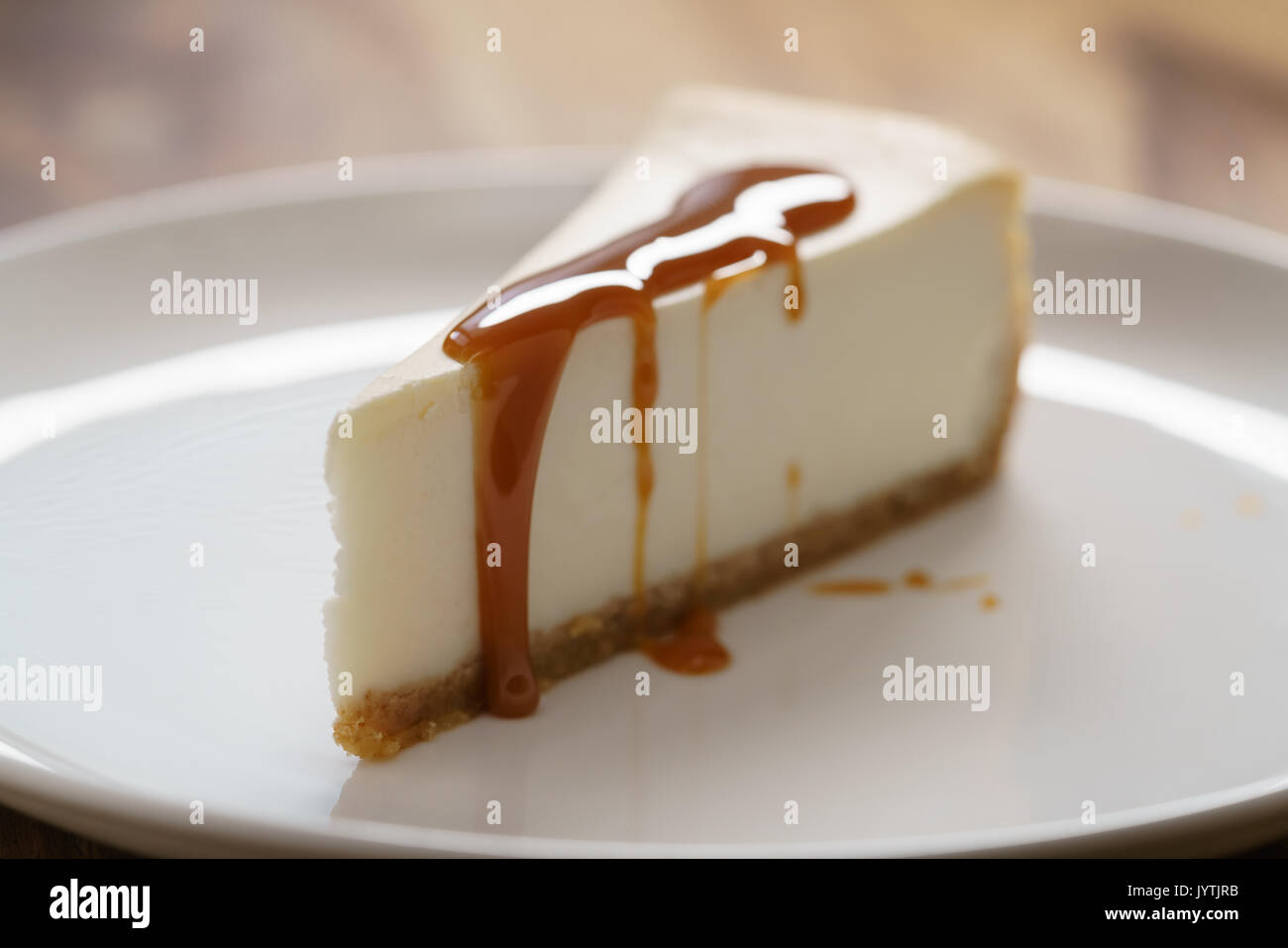 Karamellsauce auf Scheibe des traditionellen New York Cheesecake auf weiße Platte auf Holz Tabelle gegossen Stockfoto