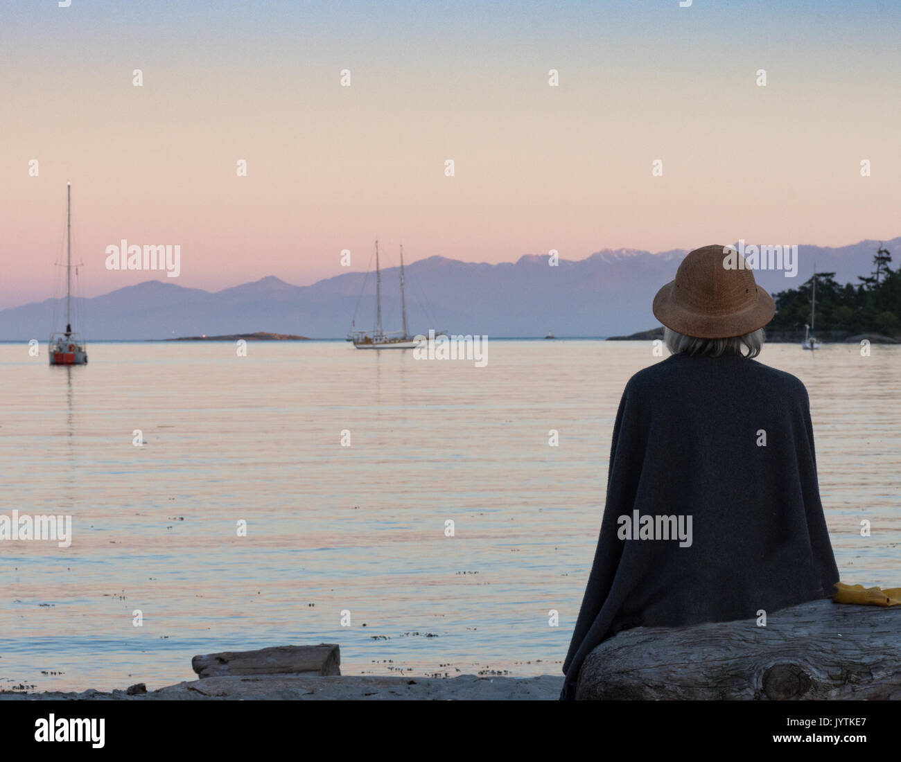 Ein grauhaariger Frau beobachten die Segelboote in der Bucht bei Sonnenuntergang. Stockfoto