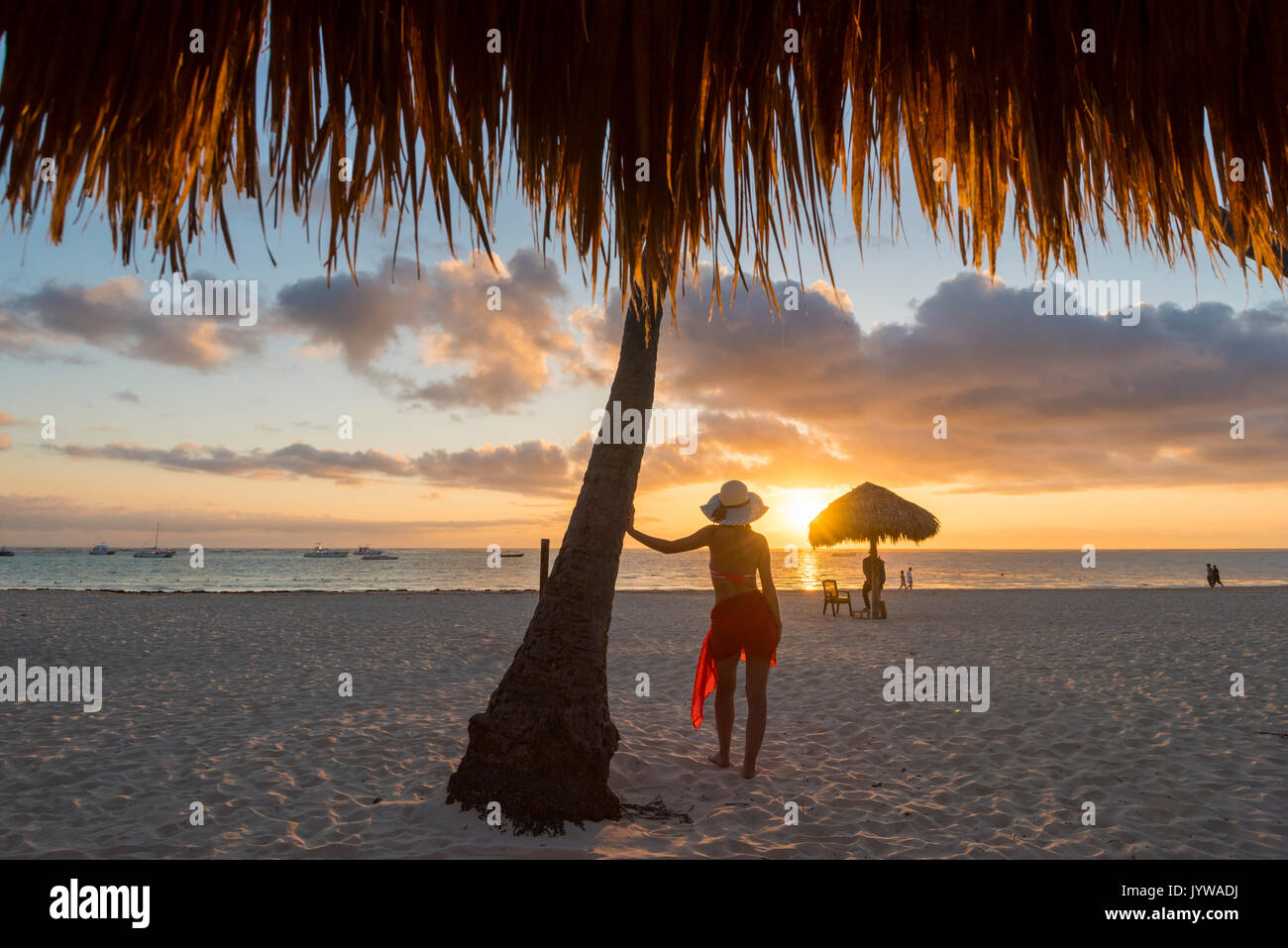Bavaro Beach, Bavaro, Higuey, Punta Cana, Dominikanische Republik. Frau von Stroh Sonnenschirme am Strand bei Sonnenaufgang (MR). Stockfoto