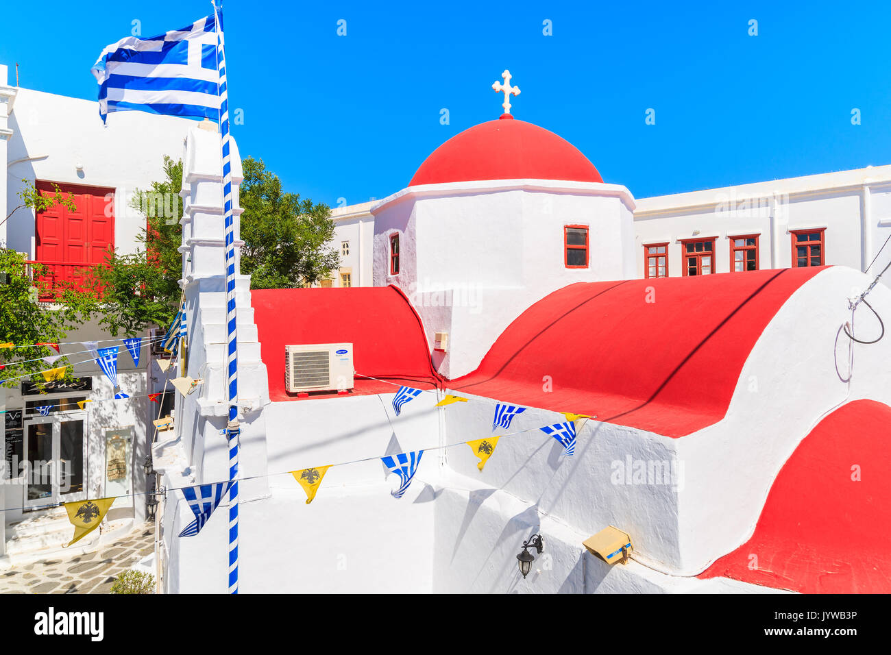 Insel Mykonos, Griechenland - 17. MAI 2016: Kirche Gebäude mit rotem Dach und die griechische Flagge auf der weiß getünchten Straße in der schönen Stadt Mykonos, Kykladen, Stockfoto
