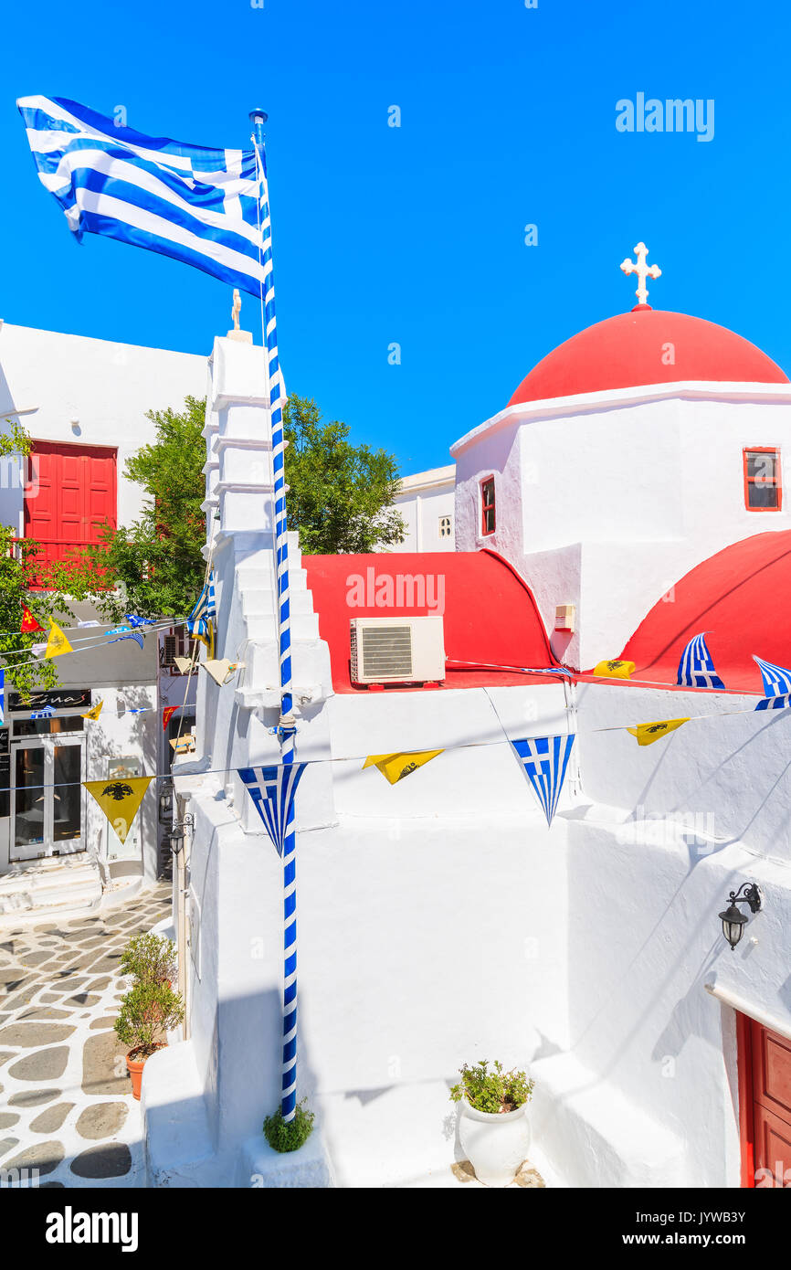 Insel Mykonos, Griechenland - 17. MAI 2016: Kirche Gebäude mit rotem Dach und die griechische Flagge auf der weiß getünchten Straße in der schönen Stadt Mykonos, Kykladen, Stockfoto