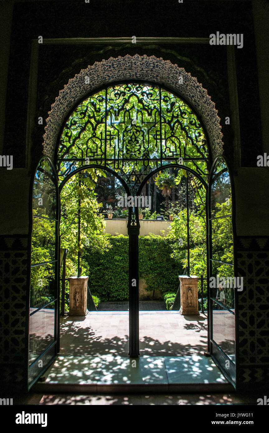 Spanien: Die Gärten des Alcazar von Sevilla, der königliche Palast herausragendes Beispiel der Mudejar Architektur, durch eine schmiedeeiserne Tür Bogen gesehen Stockfoto